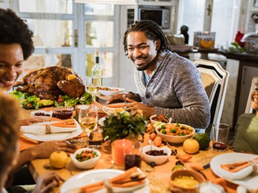A family sits around a table with Thanksgiving foods, smiling.
