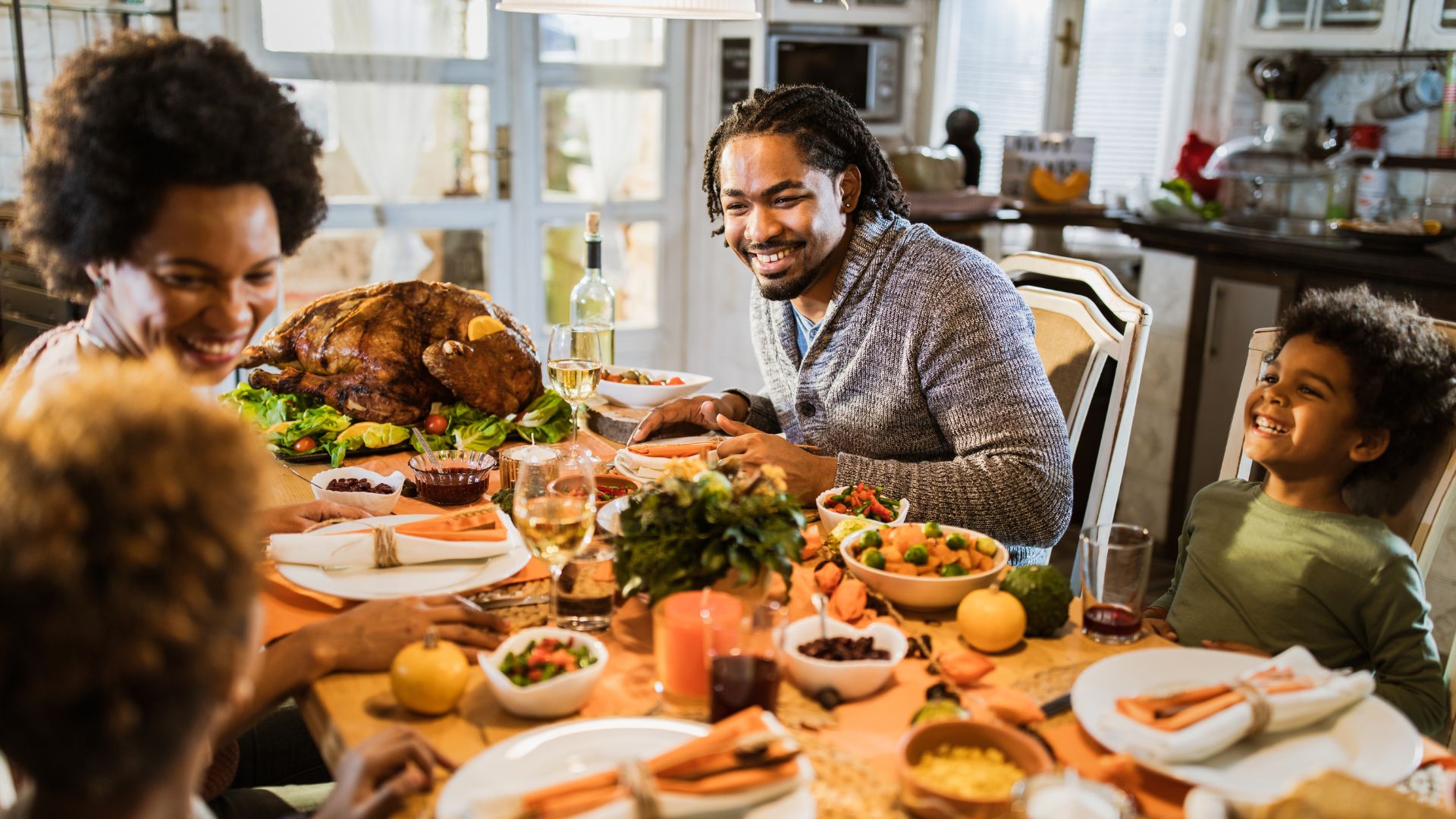 A family sits around a table with Thanksgiving foods, smiling.