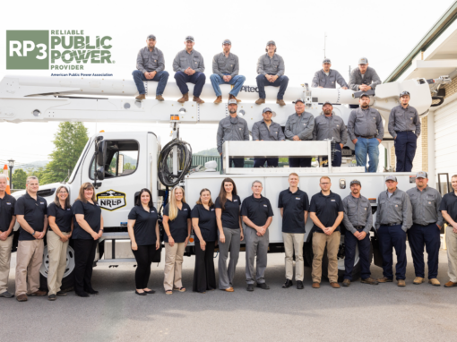 NRLP staff and lineworkers pose in front of and on top of a line truck with the RP3 logo on the top left in green.