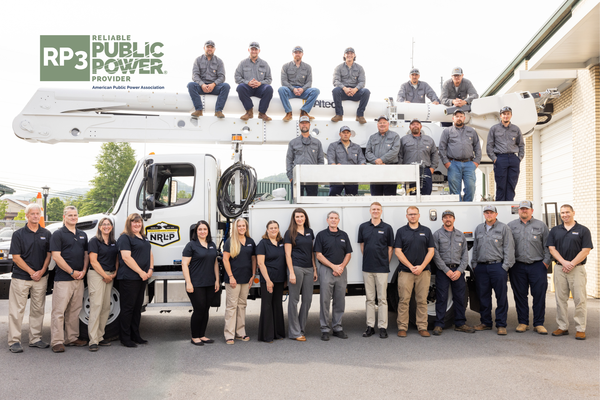 NRLP staff and lineworkers pose in front of and on top of a line truck with the RP3 logo on the top left in green.