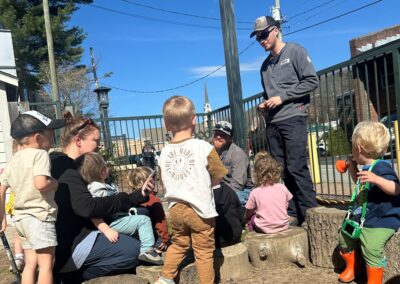 NRLP lineworkers talk with preschoolers at a local daycare on a sunny day.