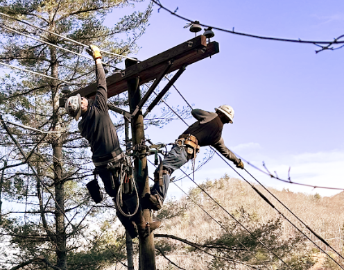 NRLP lineworkers restore power on a utility pole, pulling lines across cross arms.