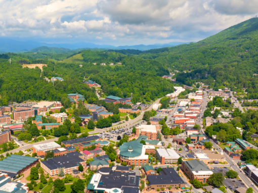 Aerial view of a portion of the town of Boone in the summer, with green-covered mountains in the background and blue skies above.