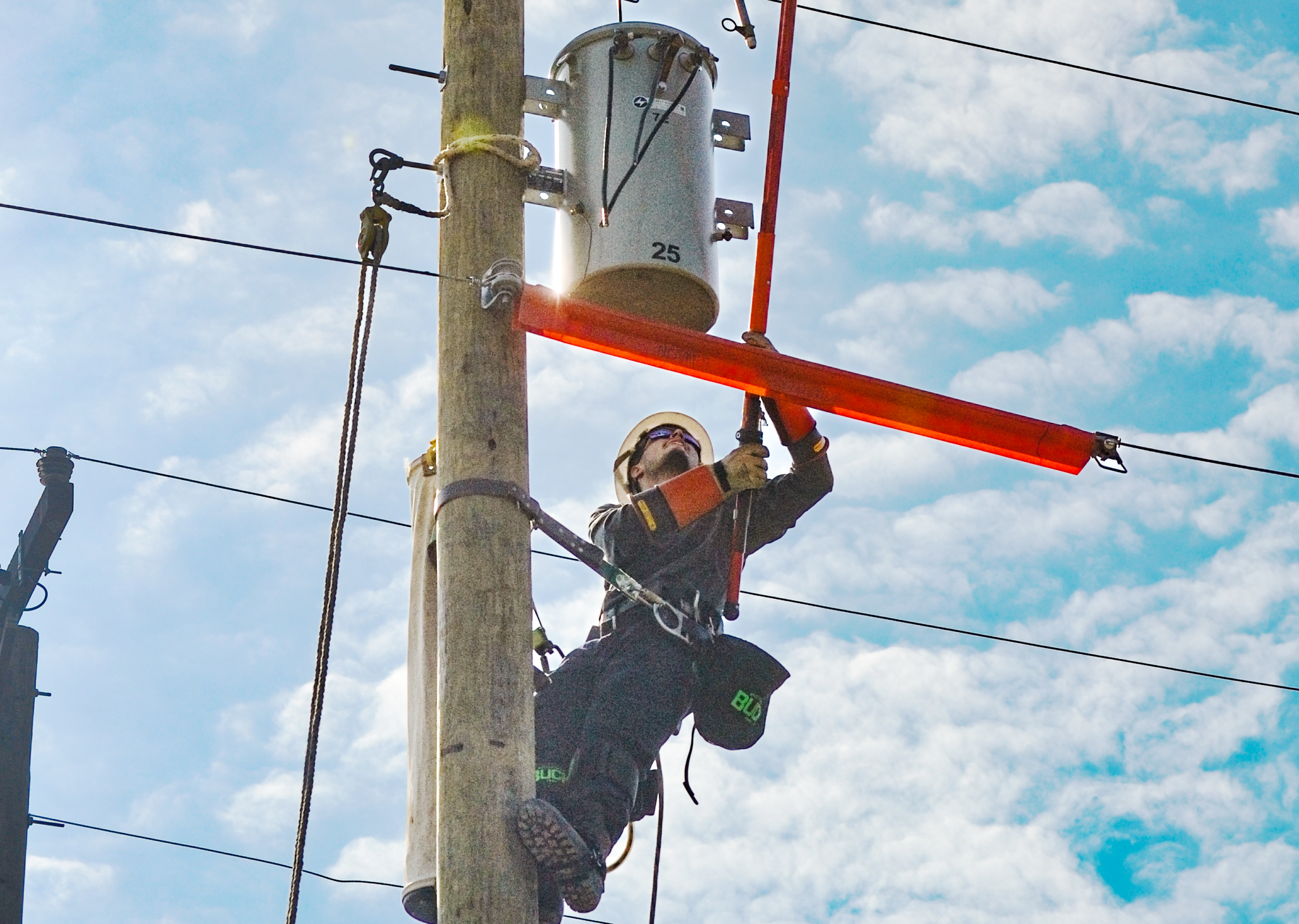 NRLP lineworker competes in lineman's rodeo transformer load switching challenge while on a utility pole using a hot stick on a sunny day with blue skies.