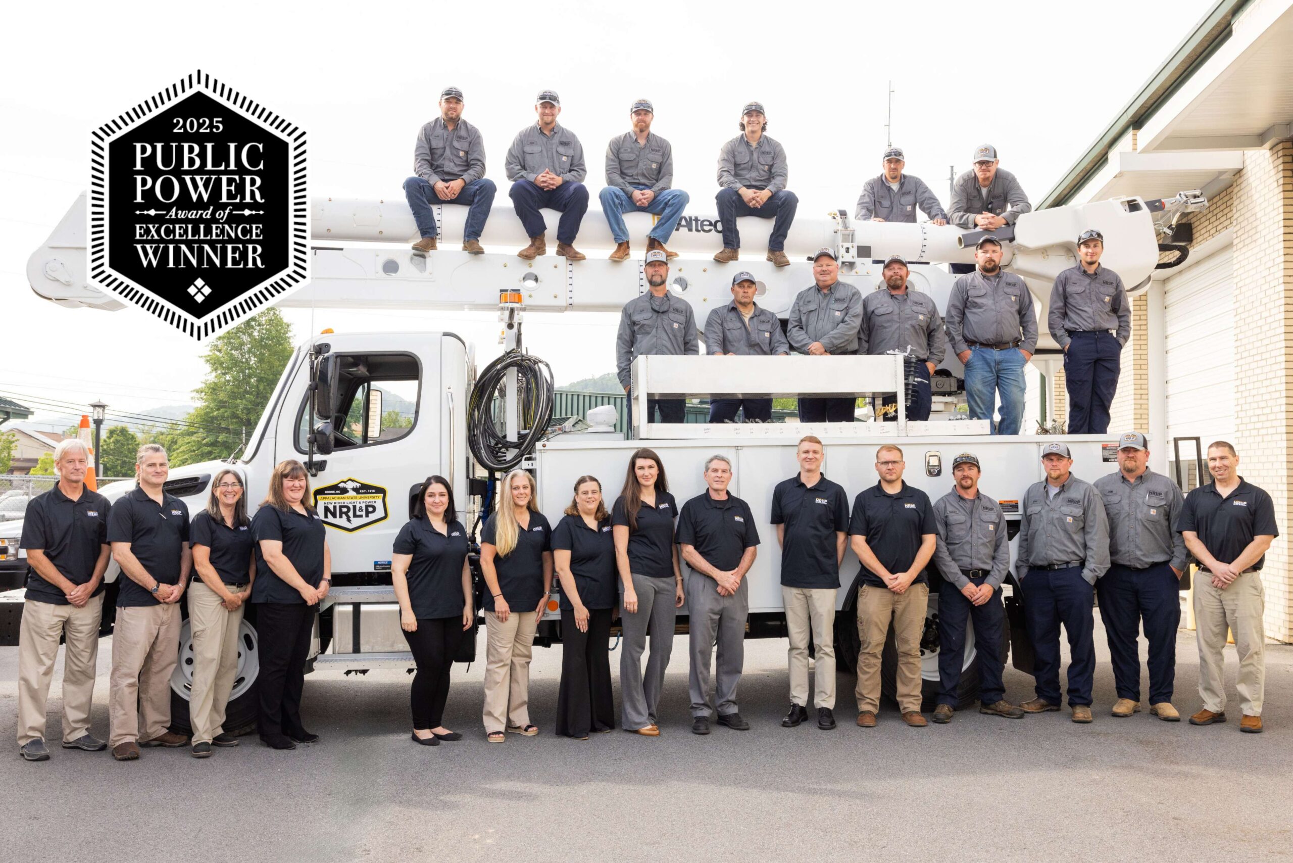 NRLP staff and crews pose for a group photo, standing in front of and sitting atop a white bucket truck.