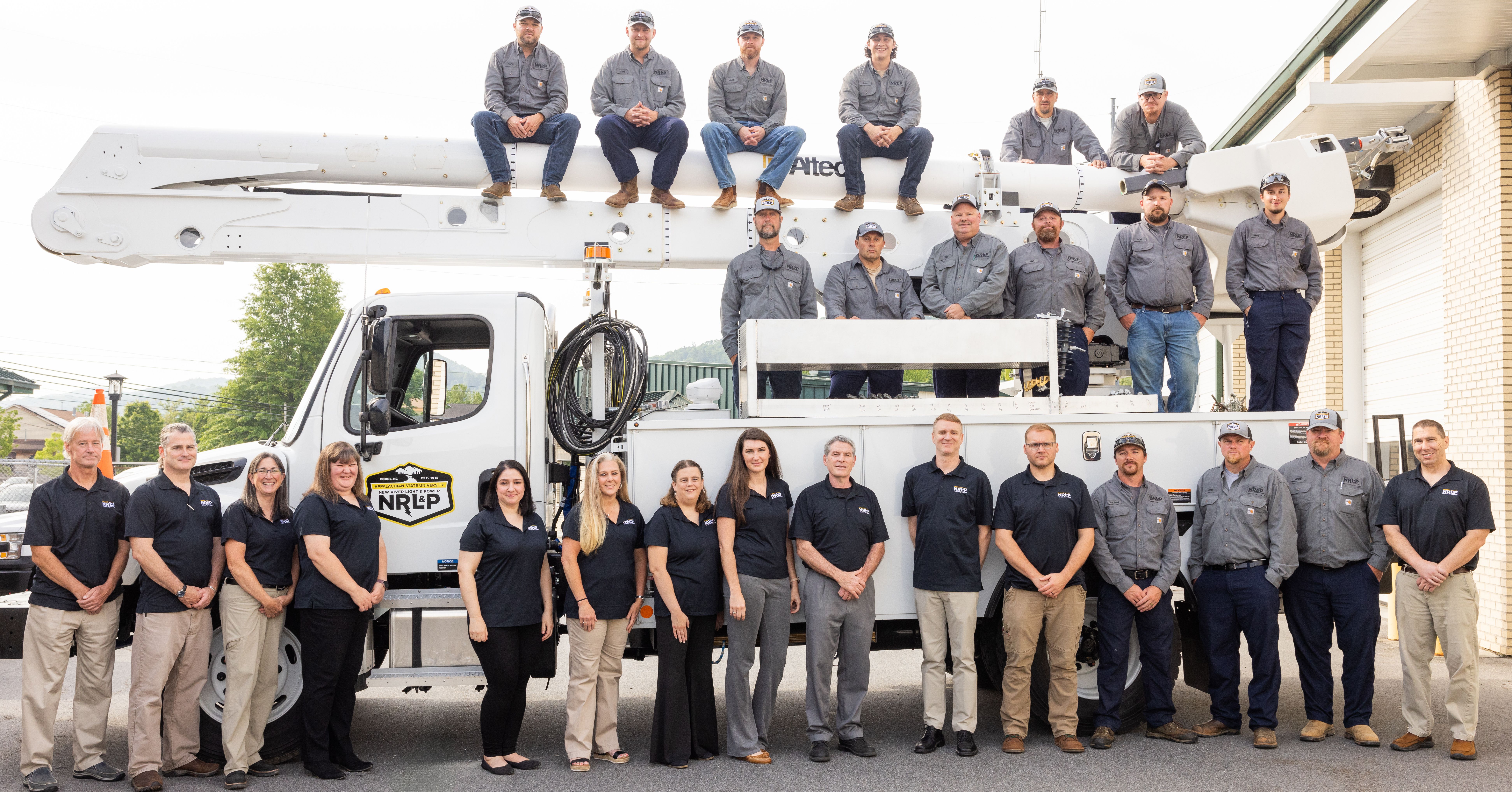 NRLP staff and lineworkers pose in front of and on top of a line truck with the RP3 logo on the top left in green.