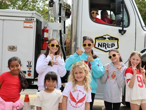 A group of students stand in front of and in a bucket truck, smiling and giving thumbs up